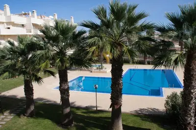 a pool with palm trees in front of a building at Vila Rosal Margarida Apartment in Albufeira