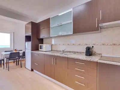 a kitchen with wooden cabinets and a table with chairs at AL - Apartamento Girassol Beach Front Quarteira in Quarteira