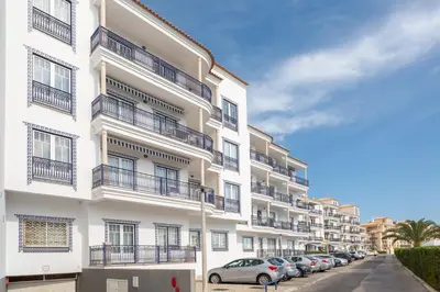 a white apartment building with cars parked in front of it at Bicos Beach Apartments By Albufeira Rental in Albufeira