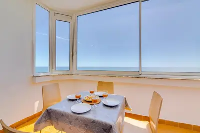 a dining room with a table and chairs and windows at AL - Apartamento Portas do Mar in Quarteira