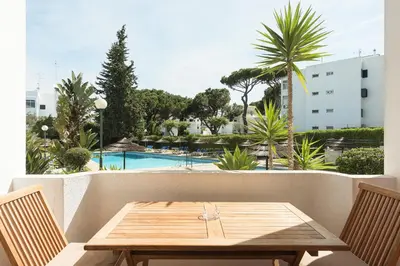 a wooden table and chairs on a balcony with a pool at Alvaflor 102 - Vilamoura by HD Properties in Vilamoura