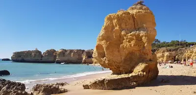 a large rock on a beach with people in the water at Sao Rafael T2 Duplex, Albufeira in Albufeira
