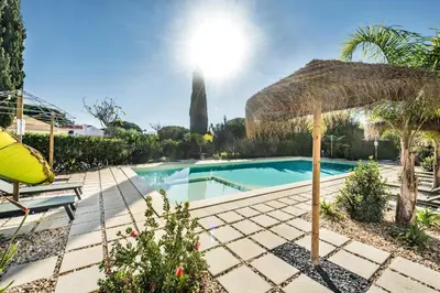 a swimming pool with a straw umbrella next to a house at Appartement Vale Lobo Mer Golf & Belle Piscine in Vale do Lobo