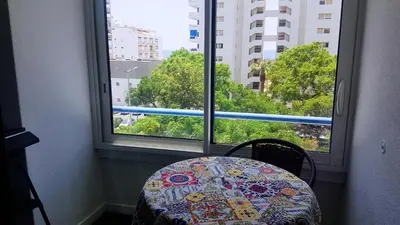 a table and chair in a room with two large windows at Studio Praia de Quarteira in Quarteira