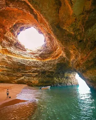 a cave on a beach with a boat in the water at Vilamoura Pine Hills Luxury Apartment in Quarteira