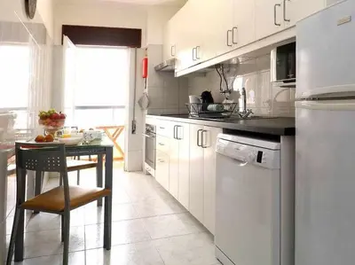 a kitchen with white cabinets and a table with a chair at Mar á vista by FHR 2 minutos á praia in Quarteira