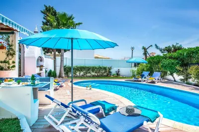 a swimming pool with chairs and a blue umbrella at Villa Toad Hall in Galé