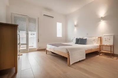 a bedroom with a large bed with white walls and wooden floors at Sunny Days beach apartment in Quarteira