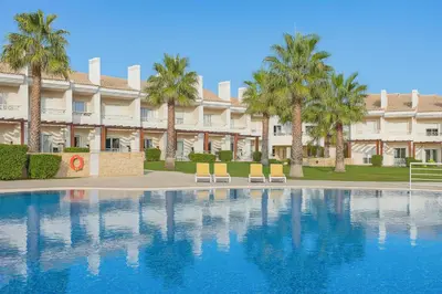 a resort with a swimming pool with two chairs and palm trees at Votre refuge en bord de mer ! in Albufeira