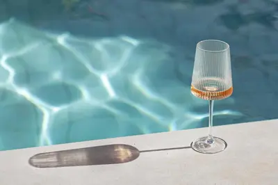 a wine glass sitting on a table next to a pool at Âmago Guesthouse in Santa Bárbara de Nexe