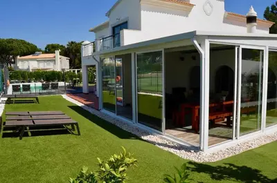 a house with large glass doors and a picnic table at Villa | w/ Private Pool, Tennis Courts & Golf Putt in Vilamoura