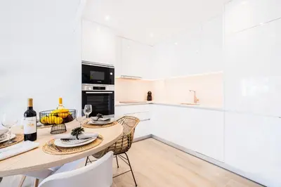 a white kitchen with a wooden table and chairs at Apartment Tanta - located at the gates of the old in Albufeira