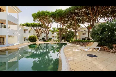a swimming pool in front of a building with trees at Falésia Modern Flat W/Balcony & Pool by LovelyStay in Albufeira