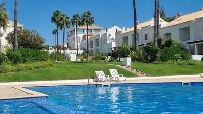 a swimming pool with two white chairs next to a building at Praia da Galé, 250m da Praia e Piscina in Galé