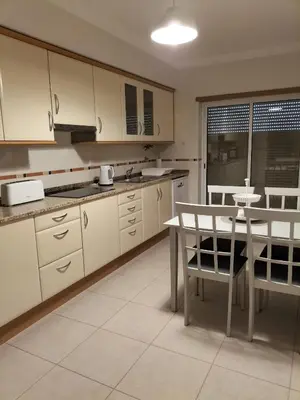 a kitchen with white cabinets and a table and chairs at T2 Infante Moderno Wi-Fi Garagem 50 M Praia in Quarteira