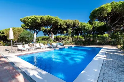 a swimming pool with chairs and umbrellas and trees at Villa Sea, Sun and Golf in Vilamoura in Quarteira