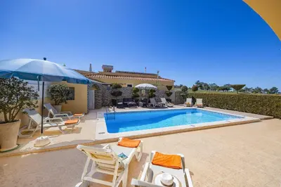 a house with a swimming pool with chairs and an umbrella at Villa Graca by Villa Plus in Albufeira