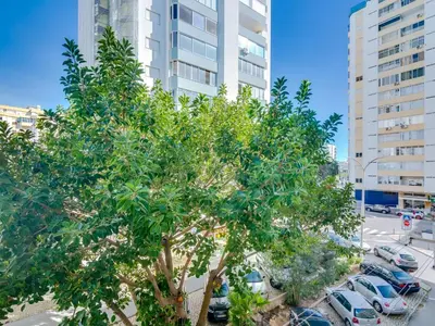 a tree in a parking lot in front of a building at AL - Beachside Hideaway Quarteira in Quarteira