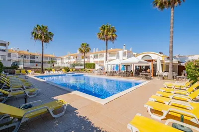a swimming pool with yellow lounge chairs and palm trees at Notre Damme Apartment in Albufeira