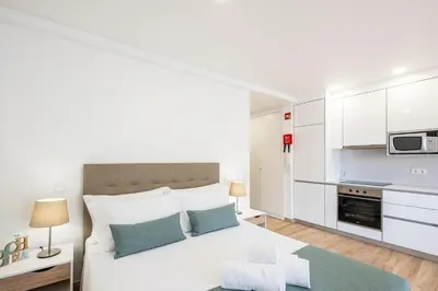 a white bedroom with a bed and a kitchen at Studio Guerreiro in Albufeira