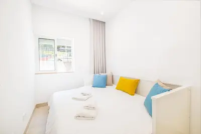a bedroom with a white bed with blue and yellow pillows at Guerreiros Lovely Stay in Albufeira