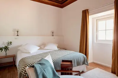 a white bedroom with a bed and a window at Solar do Bisavô in Bordeira