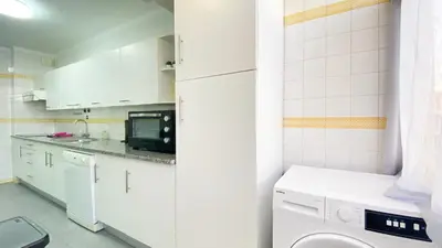 a white kitchen with a washer and a microwave at Quarteira Frente Praia II by HomeSlow Rentals in Quarteira