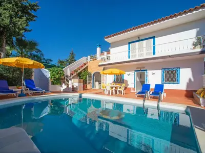 a swimming pool with chairs and umbrellas next to a house at Villa Fernandes by Interhome in Albufeira