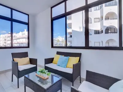 a living room with chairs and a table and windows at AL - Apartamento Quarteira Avenida in Quarteira
