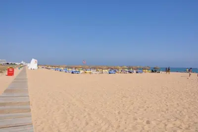 a beach with a wooden boardwalk and a group of umbrellas at Two Bedroom Laguna Village - By Vilamoura Sun in Quarteira