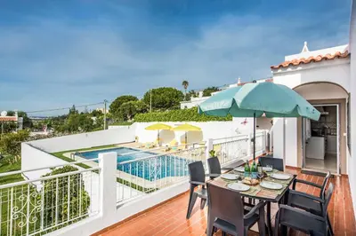 a balcony with a table and umbrella and a swimming pool at Casa Miranda in Albufeira