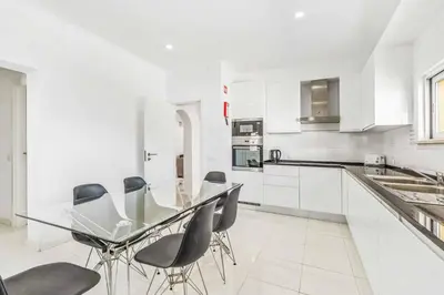 a white kitchen with a glass table and chairs at Villa Corcovada in Albufeira