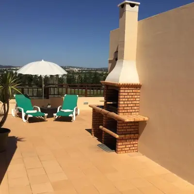 a brick fireplace on a patio with chairs and an umbrella at Apartment Rosmaninho-Hosted by Sweetstay in Quarteira