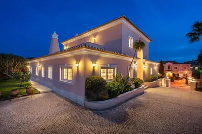 a large white house with a lighthouse in the background at Extraordinary Villa on an elevated position in Quinta do Lago in Quinta do Lago