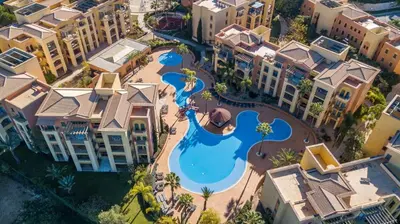 a large swimming pool with palm trees and buildings at The Prime @ The Residences Vilamoura in Quarteira