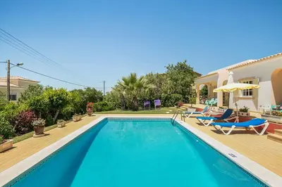 a swimming pool with chairs and a house at Villa Cerrinho in Albufeira