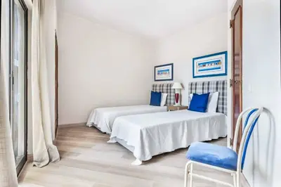 a white bedroom with two beds and a chair at Villa Silveira II in Vilamoura