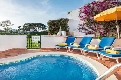 a swimming pool with blue chairs and an umbrella at Mng Elliott42 in Vale do Lobo