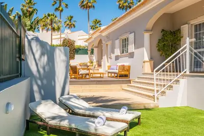 a house with two chairs and a porch with palm trees at Vicente Mar Luxury Villa - Private Pool in Albufeira