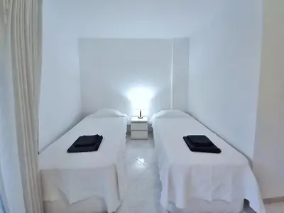 two beds in a room with white walls and a lamp at Beachfront flat with pool in Quarteira