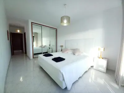 a white bedroom with a large bed and a mirror at Beachfront flat with pool in Quarteira