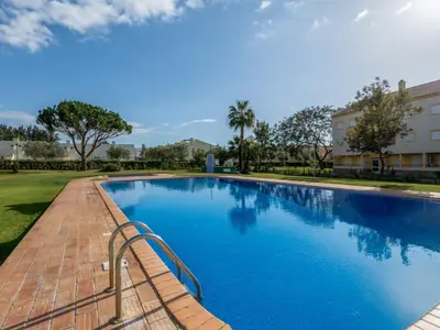 a large swimming pool with a brick walkway next to a building at Apartment T2 Cassias VIP Properties by Interhome in Vilamoura