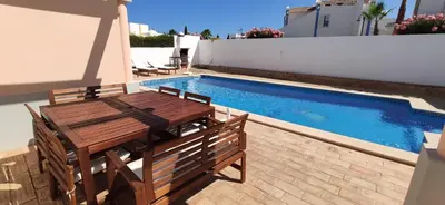 a wooden table and chairs next to a swimming pool at Casa Golfinho, Albufeira in Albufeira