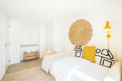 a white bedroom with a white couch and a fan on the wall at Casa na Muralha - Beach front - Rooftop Jacuzzi by DreamvillasAlbufeira in Albufeira