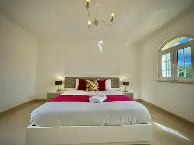 a white bedroom with a large bed with red pillows at Quarteira Premium Villa With Pool by Homing in Quarteira