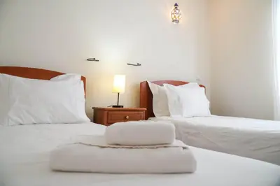 two beds with white pillows and a table with a lamp at Villa Lychee in Guia
