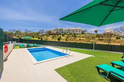 a patio with a swimming pool and a green umbrella at Villa Krishan Albufeira - Private Pool in Albufeira