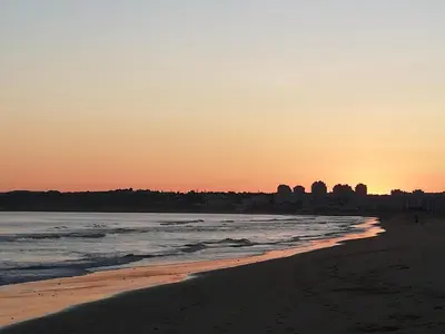 a beach at sunset with a city in the background at Casa ARRIFES in Albufeira