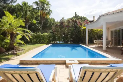 a swimming pool with two chairs and a house at Vila Caraibas - Vilamoura - by HDproperties in Vilamoura
