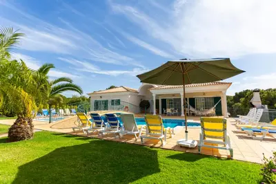 a group of chairs and an umbrella next to a pool at Exceptional Villa with Pool, Tennis Court, Games Room in Quarteira